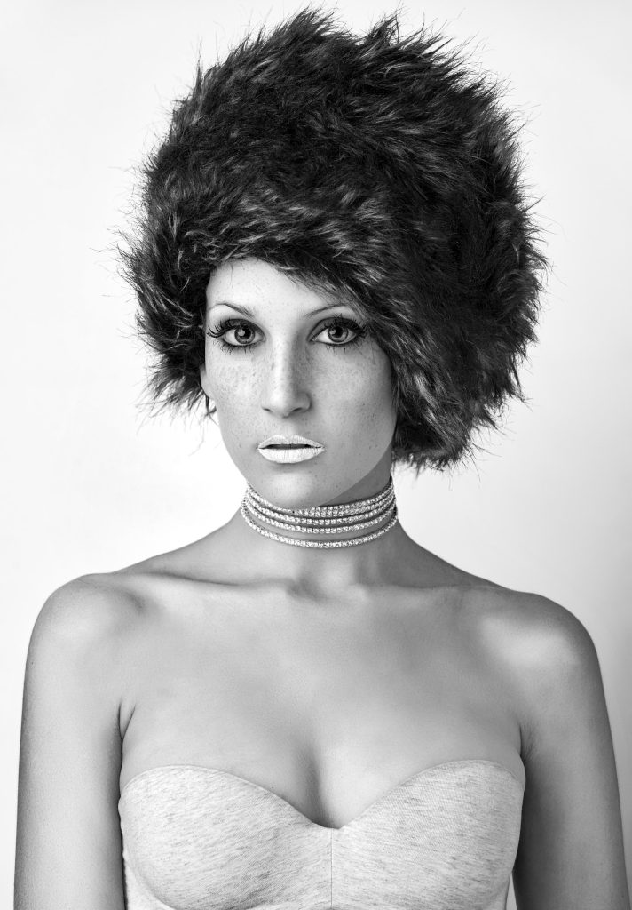 Sesión fotográfica de estudio de modelo con gorro de pelo y aros en el cuello en blanco y negro, fotografía de Rubén Casado